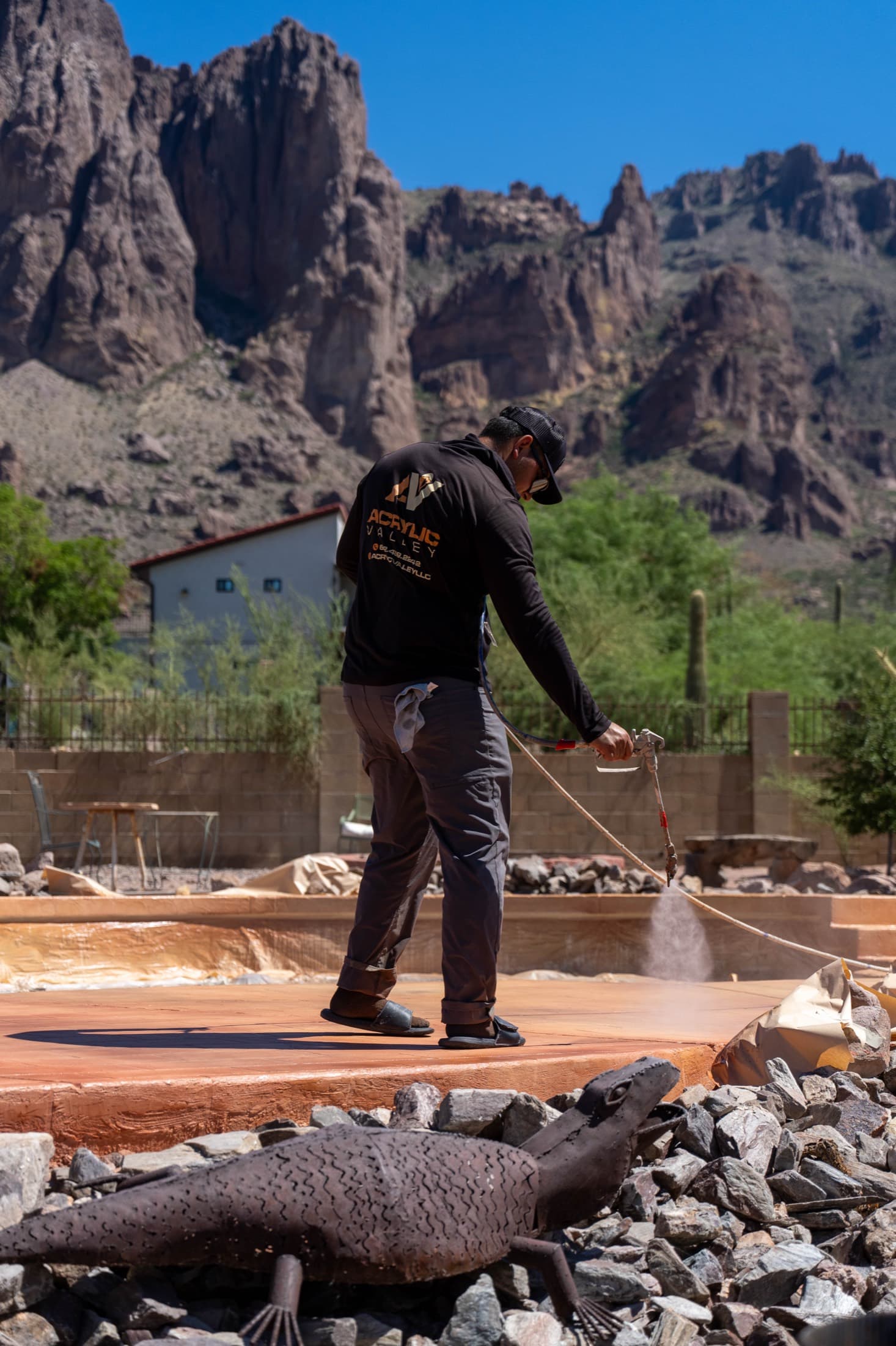 Acrylic Valley crew member spraying sealer along the edge of a terracotta pool deck